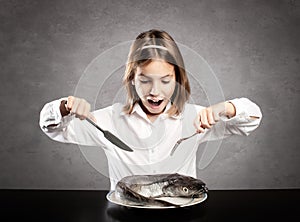 Little hungry girl in front of a whole raw fish