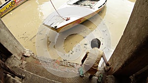 Little indian boy goes by bare feet about muck near by cows comes to dirty water of holy river Ganges and wash his slippers wooden