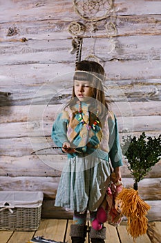 Little indian girl holding a doll and feathers in her hands. dreamcatcher. wooden background