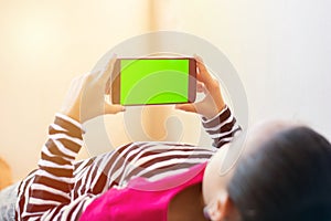 Little Indian Kid with phone in her hands sleeping on bed, mock up with green screen, focus on phone.