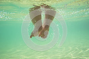 Happy baby steps, underwater view. .Little infant baby child legs and toes touch sand on sea beach