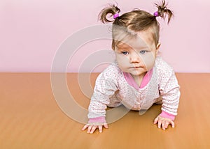 Little an infant girl with ponytails on the head crawling on the floor.