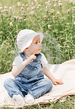 A little infante girl in a white cap sits in the park among the flowers