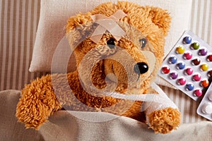 Little injured teddy bear lying sick in bed