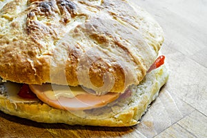 Little italian focaccia bread stuffed with turkey ham, red bell peppers, cheese and red onions on wooden cutting board