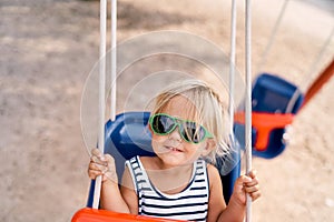 Little joyful girl in sunglasses on a swing