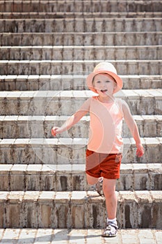 The little joyful girl went down the stairs. A child wearing a stylish hat and red shorts.