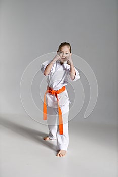 A little karate girl in a white kimono in a fighting stance