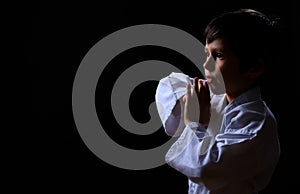 Little karate kid in white kimono isolated on dark background. Portrait of boy ready for martial arts fight. Child fighting at