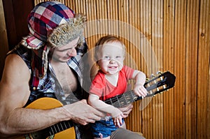 Little kid baby with his hipster father playing guitar on wooden background