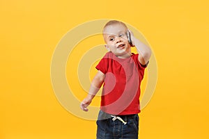 Little kid boy 3-4 years old in red t-shirt talking on mobile phone, conducting pleasant conversation isolated on yellow