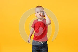 Little kid boy 3-4 years old in red t-shirt talking on mobile phone, conducting pleasant conversation isolated on yellow