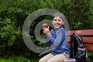 Little kid boy with backpack eating fresh apple on a street