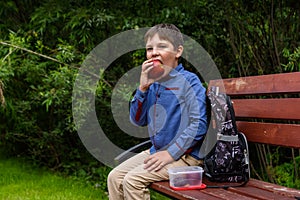 Little kid boy with backpack eating fresh apple on a street