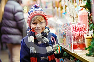 Little kid boy with candy cane stand on Christmas market