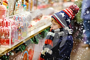 Little kid boy with candy cane stand on Christmas market