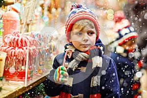 Little kid boy with candy cane stand on Christmas market