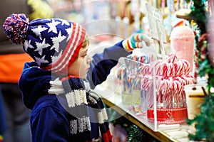 Little kid boy with candy cane stand on Christmas market