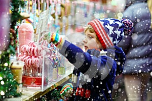 Little kid boy with candy cane stand on Christmas market