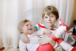 Little kid boy comforts his adorable crying baby sister. Sad toddler girl and lovely brother indoors at home. Girl hit