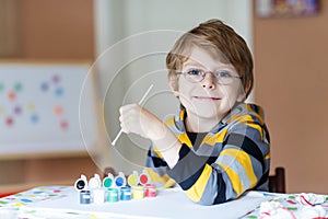 Little kid boy drawing with colorful watercolors indoors