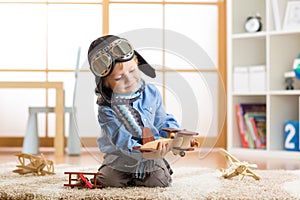 Little kid boy dreams be an aviator and plays with toy airplanes sitting on floor in nursery room