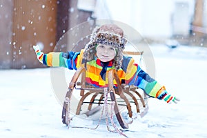 Little kid boy enjoying sleigh ride during snowfall. Happy preschool kid riding on vintage sledge.