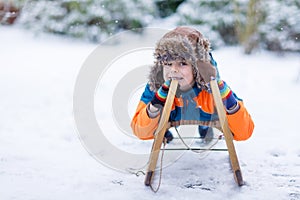 Little kid boy enjoying sleigh ride during snowfall. Happy preschool kid riding on vintage sledge. Child play outdoors