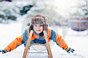 Little kid boy enjoying sleigh ride during snowfall. Happy preschool kid riding on vintage sledge. Child play outdoors