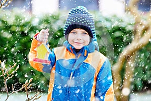 Little kid boy hanging bird house on tree for feeding in winter