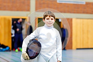 Little kid boy fencing on a fence competition. Child in white fencer uniform with mask and sabre. Active kid training