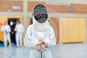 Little kid boy fencing on a fence competition. Child in white fencer uniform with mask and sabre. Active kid training