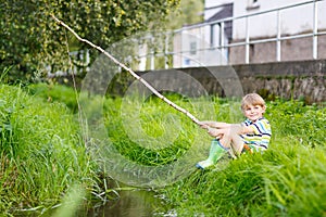 Little kid boy fishing on river with selfmade fishing rod