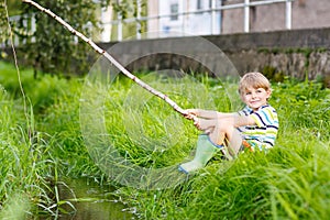 Little kid boy fishing on river with selfmade fishing rod