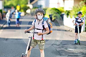 Little kid boy with glasses with medical mask on the way to school with scooter. Child with satchel. Schoolkid. Lockdown