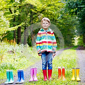 Little kid boy and group of colorful rain boots. Blond child standing in autumn forest. Close-up of schoolkid and