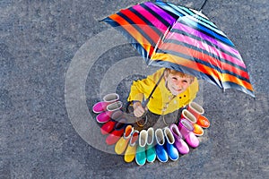 Little kid boy and group of colorful rain boots. Blond child standing under umbrella. Close-up of schoolkid and