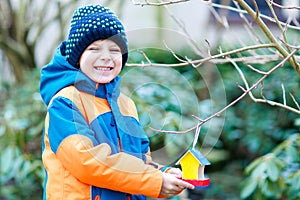 Little kid boy hanging bird house on tree for feeding in winter