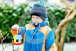 Little kid boy hanging bird house on tree for feeding in winter