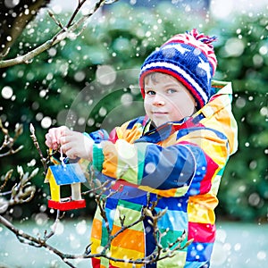Little kid boy hanging bird house on tree for feeding in winter
