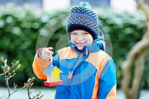 Little kid boy hanging bird house on tree for feeding in winter