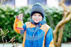 Little kid boy hanging bird house on tree for feeding in winter