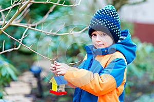 Little kid boy hanging bird house on tree for feeding in winter