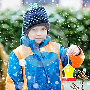 Little kid boy hanging bird house on tree for feeding in winter