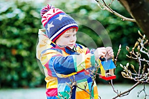 Little kid boy hanging bird house on tree for feeding in winter