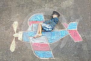 Little kid boy having fun with with airplane picture drawing with colorful chalks on asphalt. Child painting with chalk