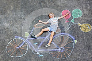 Little kid boy having fun with bicycle chalks picture on ground