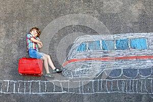 Little kid boy having fun with fast train picture drawing with colorful chalks on asphalt