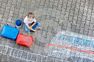 Little kid boy having fun with fast train picture drawing with colorful chalks on asphalt