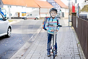 Little kid boy in helmet riding with his scooter in the city